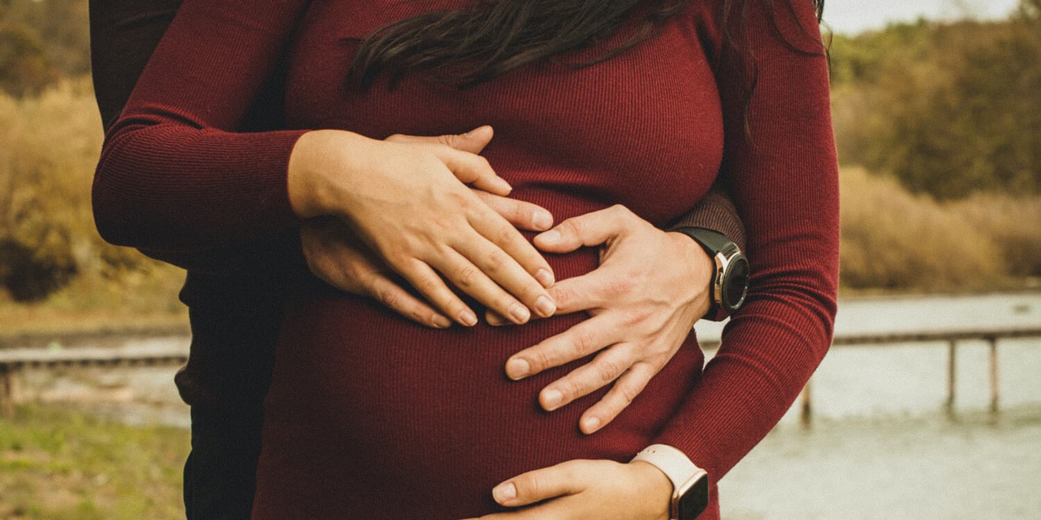 Pregnant couple outdoors and both embrace the woman's baby bump 