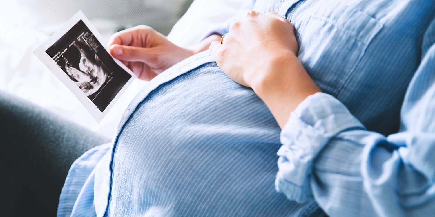 Pregnant woman holds ultrasound image in one hand and has her other hand on her belly